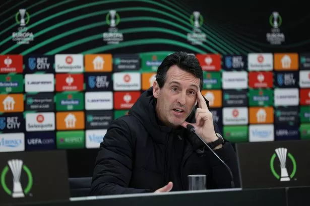 Unai Emery looks pensive during a Conference League press conference, with a sponsors' hoarding behind him.