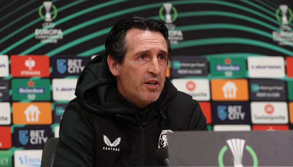 Unai Emery, photographed from below, looking out at a crowd of journalists who are out of shot. He is wearing a black Castore hoodie.